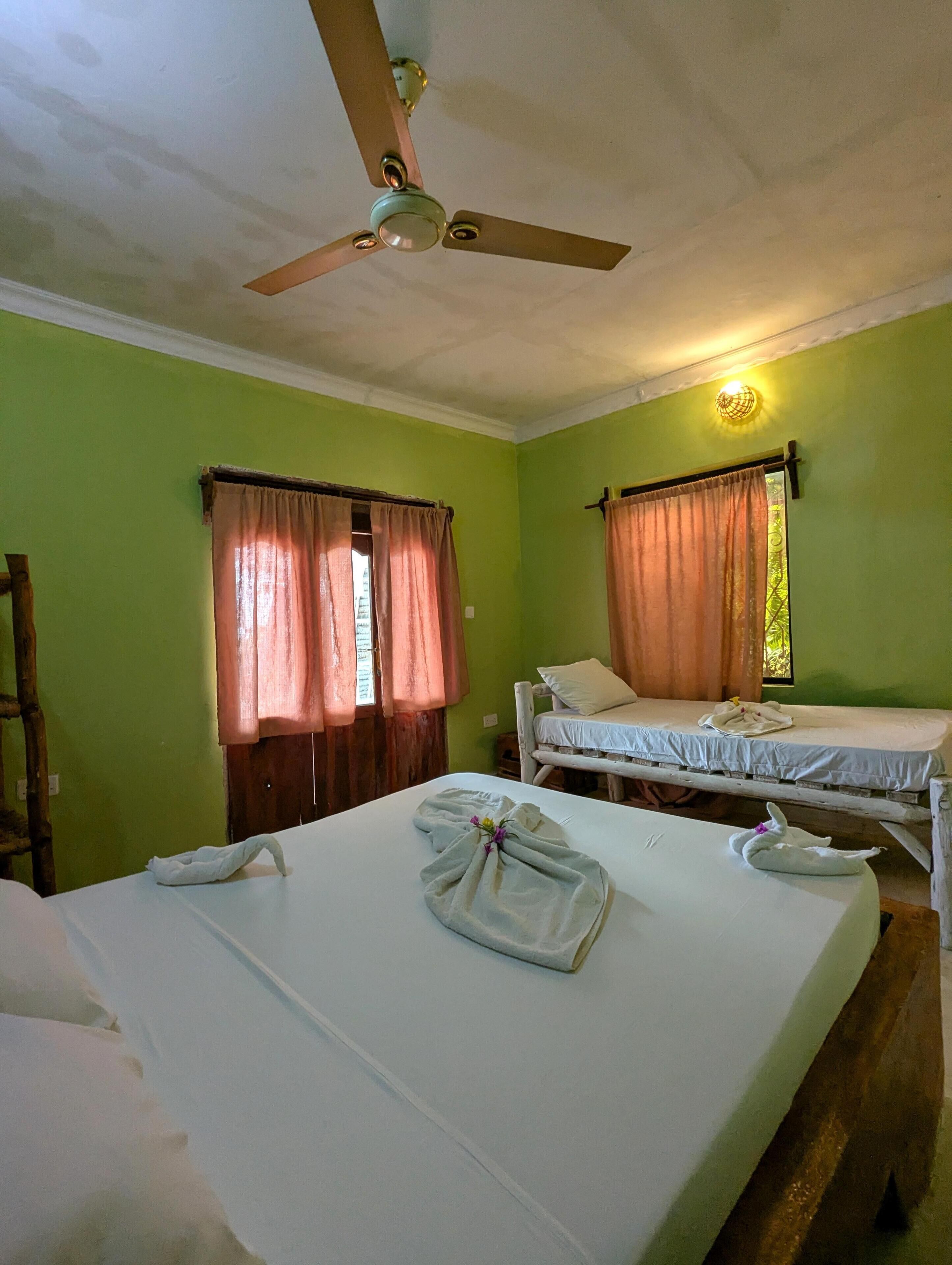 Una habitación con dos camas, ventilador de techo y ventana con cortinas.