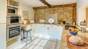 A kitchen with a stone wall, built-in ovens, a wooden ceiling, and a marble countertop. - 4 Bed in Oakham (oc-86556) (Empingham)