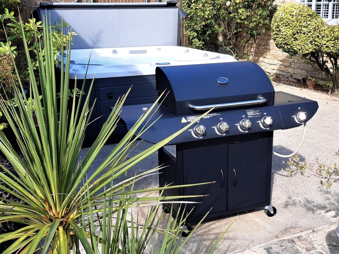 A black barbecue grill with four burners and a digital display, positioned on a concrete patio with a plant in the foreground.