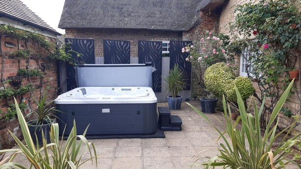A hot tub in a courtyard with potted plants and a brick wall. - 4 Bed in Oakham (oc-86556) (Empingham)