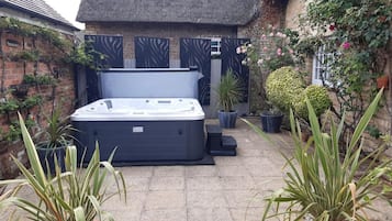 A hot tub in a courtyard with potted plants and a brick wall.