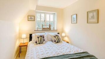 A bedroom with a bed, two bedside tables, a window, and three framed pictures on the wall.
