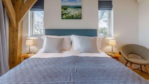 Um quarto com uma cama, duas luminárias de cabeceira, uma cadeira e um quadro na parede.