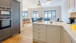 Una cocina moderna con hornos empotrados, una isla central con cajones, iluminación colgante y vistas a un comedor.