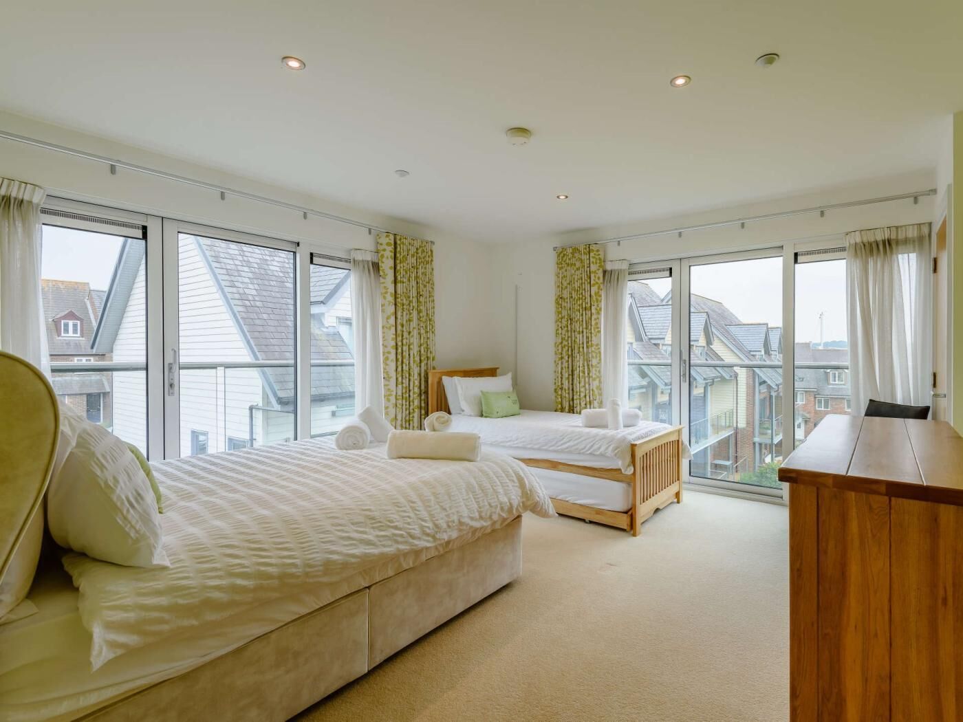 A bedroom with two beds, large windows, and a view of the outside.