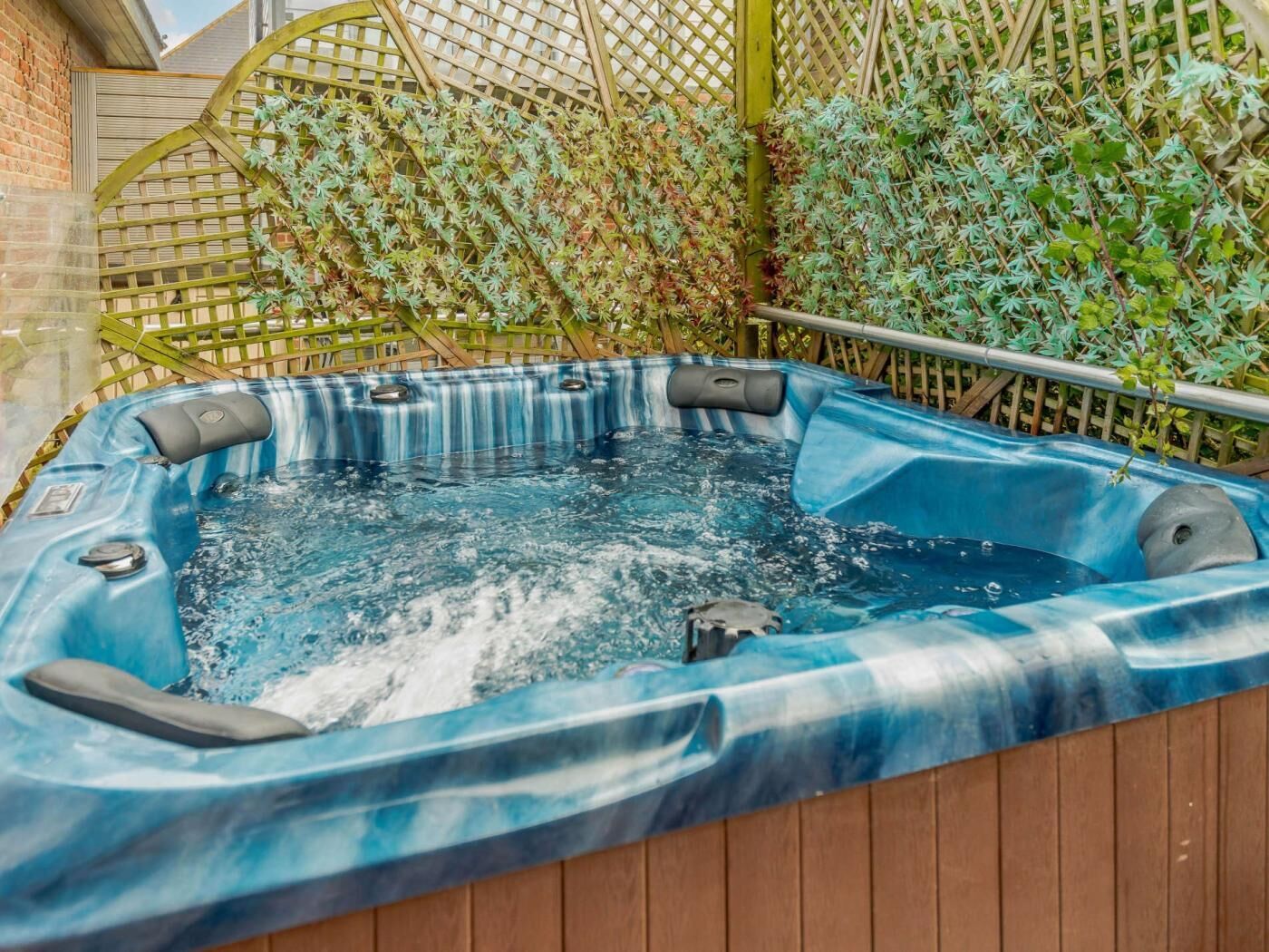 Un bain à remous avec une terrasse en bois et une clôture en treillis en arrière-plan.