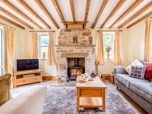 A cozy living room with a stone fireplace, wooden beams, a sofa, a TV, and a coffee table.