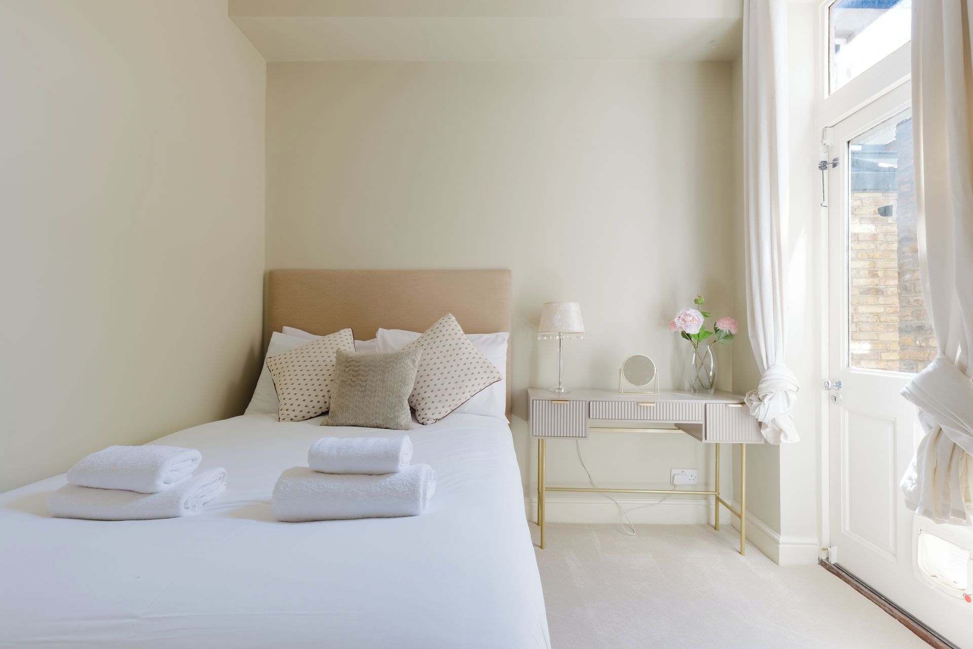 Une chambre d’hôtel avec un lit, une table de chevet, une lampe, des fleurs et une vue sur l’extérieur.