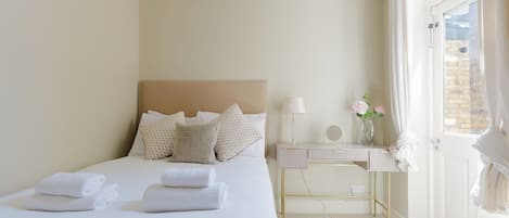 A hotel room with a bed, bedside table, lamp, flowers, and a view of the outside.
