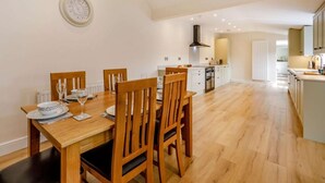 A dining area with a wooden table and chairs, a kitchen in the background, and a clock on the wall. - 3 Bed in Bedale (oc-88242) (Snape)