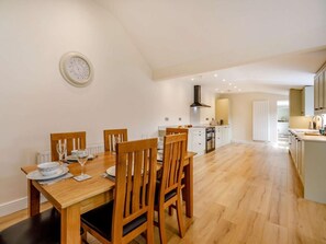 A dining area with a wooden table and chairs, a kitchen in the background, and a clock on the wall. - 3 Bed in Bedale (oc-88242) (Snape)