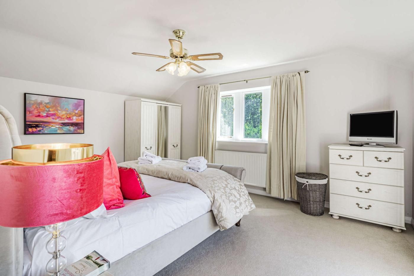 A bedroom with a bed, a ceiling fan, a television, a dresser, and a window with curtains.