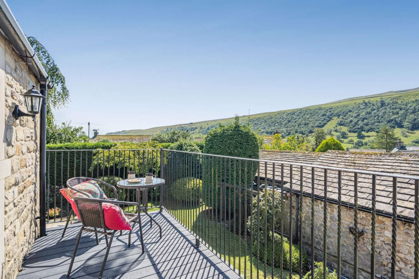 A balcony with a table and chairs, a stone wall, and a view of a green landscape.