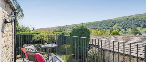 A balcony with a table and chairs, a stone wall, and a view of a green landscape.