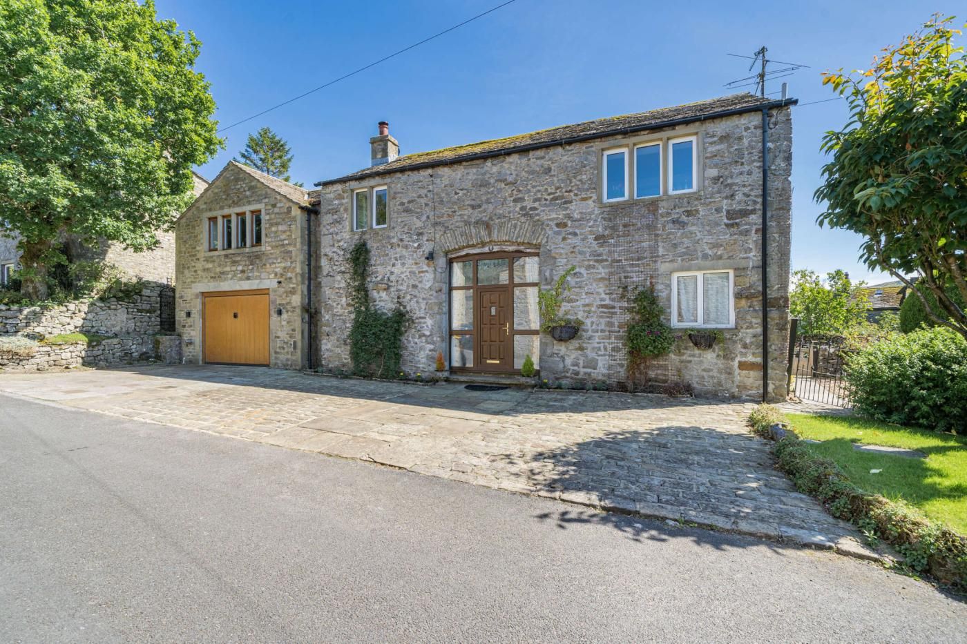 A stone house with a wooden door, a garage, and a paved driveway.