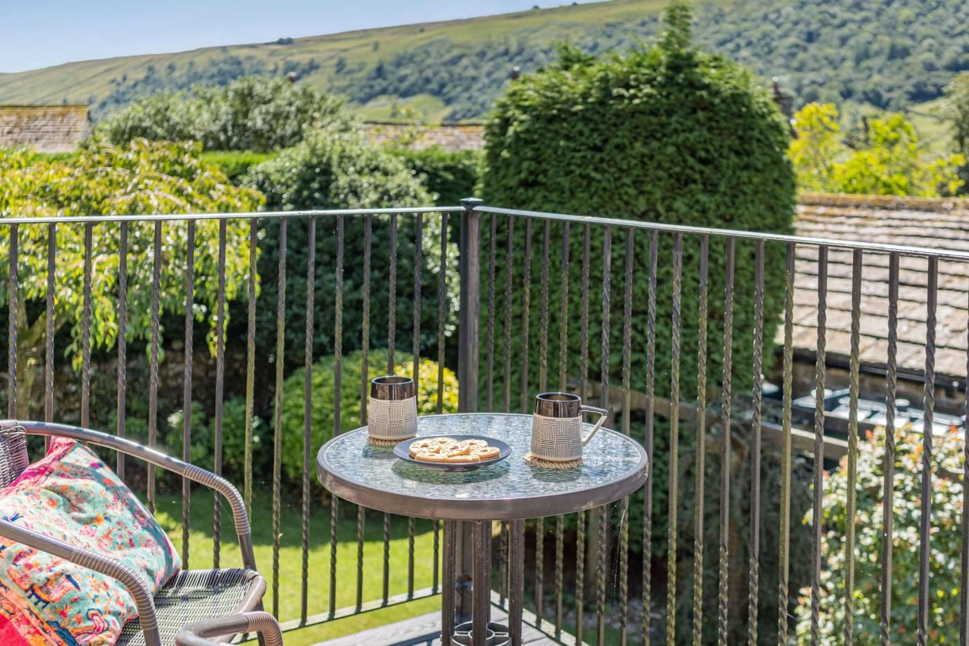 A balcony with a round table, two metal cups, and a colorful cushion.