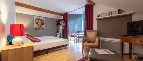 Habitación de hotel con cama, escritorio con televisor, silla, alfombra roja y estantería.