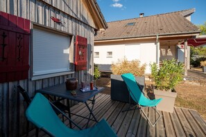 Eine Holzterrasse mit Tisch und Stühlen, einem roten Briefkasten und einem weißen Gebäude im Hintergrund.