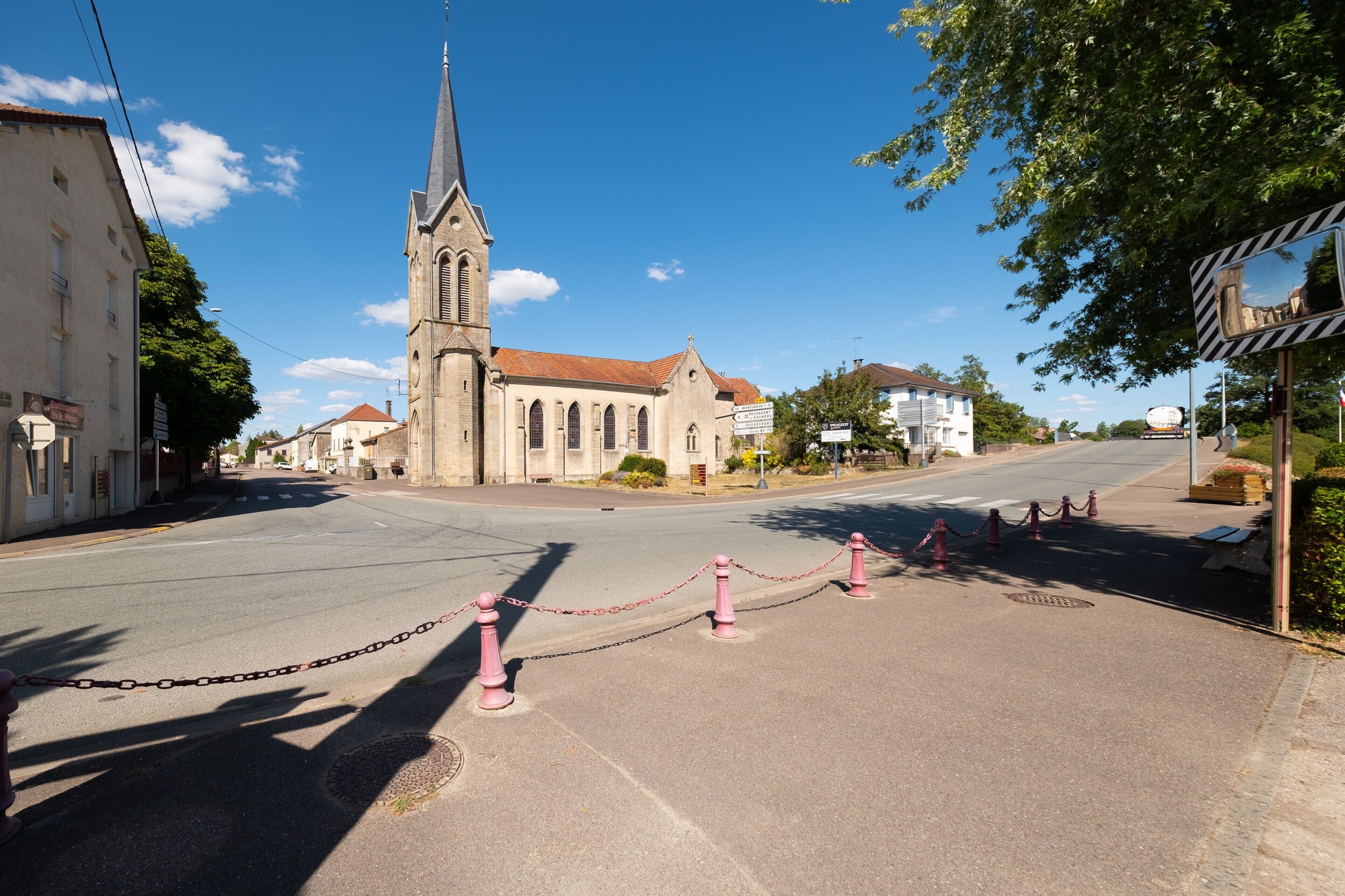 A church with a tall spire, a chain-locked area in the foreground, and a clear blue sky.