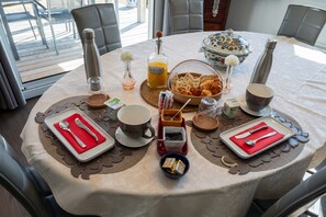 Desayuno preparado para dos, con platos, cubiertos, tazas y un bol de pastelería.