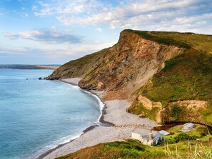 Un paysage côtier avec une plage, des falaises et un petit bâtiment.