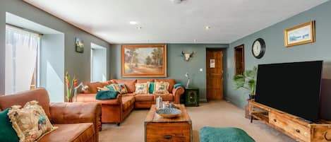 A living room with a brown leather sofa, a wooden coffee table, a television on a wooden stand, and a large painting on the wall.