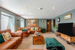 Un salon avec un canapé en cuir marron, une table basse en bois, un téléviseur posé sur un meuble en bois et un grand tableau accroché au mur.
