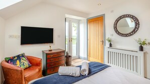 A bedroom with a bed, a TV, a dresser, a chair, a mirror, and a door leading outside. - 6 Bed in Holsworthy (oc-89218) (Holsworthy Hamlets)