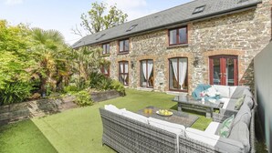 A stone building with a patio, outdoor furniture, and a well-maintained lawn. - 6 Bed in Holsworthy (oc-89218) (Holsworthy Hamlets)
