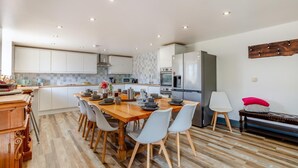 A modern kitchen with white cabinets, a wooden dining table, and a built-in oven. - 6 Bed in Holsworthy (oc-89218) (Holsworthy Hamlets)