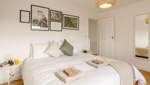 Un dormitorio con cama, almohadas, una mesita de noche con un vaso de jugo de naranja y una pared decorada con cuadros.