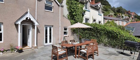 A patio area with a table and chairs, a barbecue grill, and a view of the surrounding neighborhood.