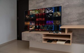 A modern living room with a large flat-screen TV mounted on a wall, a wooden coffee table, and a built-in shelf with a projector. - Corporate Stays Insignia 4 - A63 (Lúke)