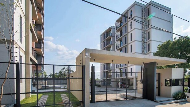 Un moderno edificio de apartamentos con entrada protegida, un corredor cubierto y un balcón visible en el lado izquierdo.