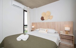 Habitación de hotel con cama, dos mesitas de noche, unidad de aire acondicionado, ventana con cortinas y un adorno en la pared.