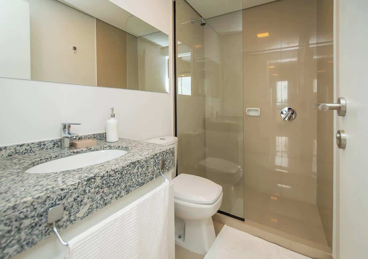 A bathroom with a granite countertop sink, a toilet, a glass-enclosed shower, and a mirror above the sink.