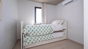 Una cama individual con una colcha estampada, una ventana con cortinas y un aire acondicionado.