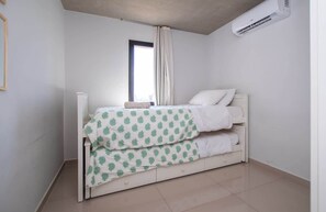 A single bed with a patterned bedspread, a window with curtains, and an air conditioning unit. - Corporate Stays Insignia 4 - A63 (Lúke)