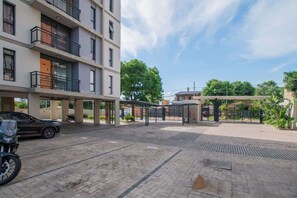 Un edificio residencial de varios pisos con balcones, zona de estacionamiento techada y entrada protegida por un portón.