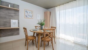 Un comedor con una mesa redonda, cuatro sillas de madera, un florero con plantas y láminas botánicas enmarcadas en la pared.