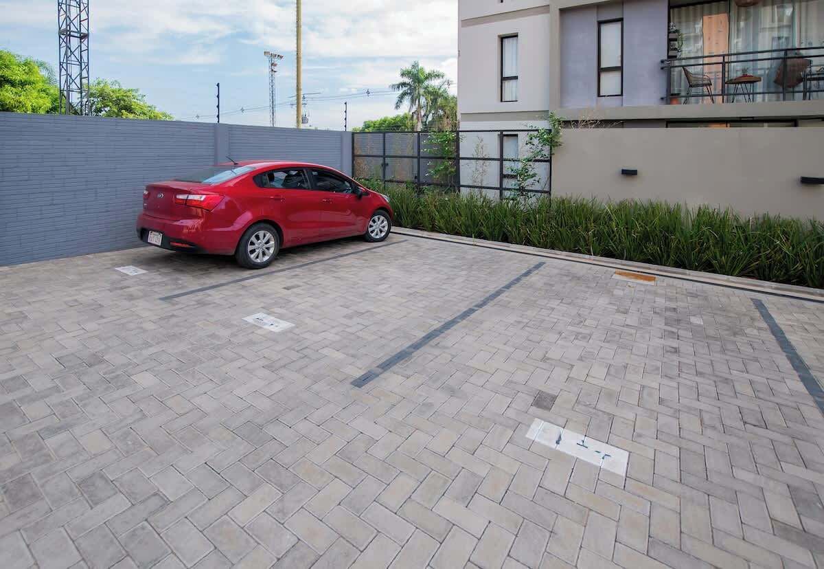 A red car parked in a paved parking area with a building in the background.