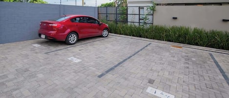 A red car parked in a paved parking area with a building in the background.
