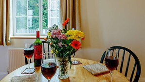 Et bord med vinglas, en flaske og en vase med blomster ved et vindue.