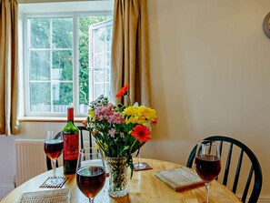 A table with wine glasses, a bottle, and a vase with flowers by a window. - 2 Bed in Abergele (oc-89413) (Betws-yn-Rhos)