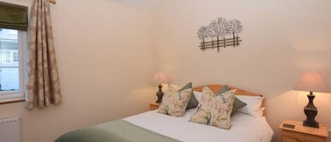A bedroom with a bed, two bedside tables, a radiator, a window with curtains, and a wall decoration.