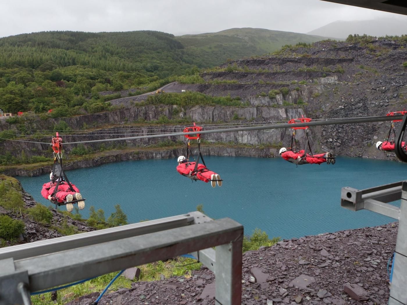 A cable car system with passengers in red harnesses over a body of water, surrounded by rocky terrain and greenery.