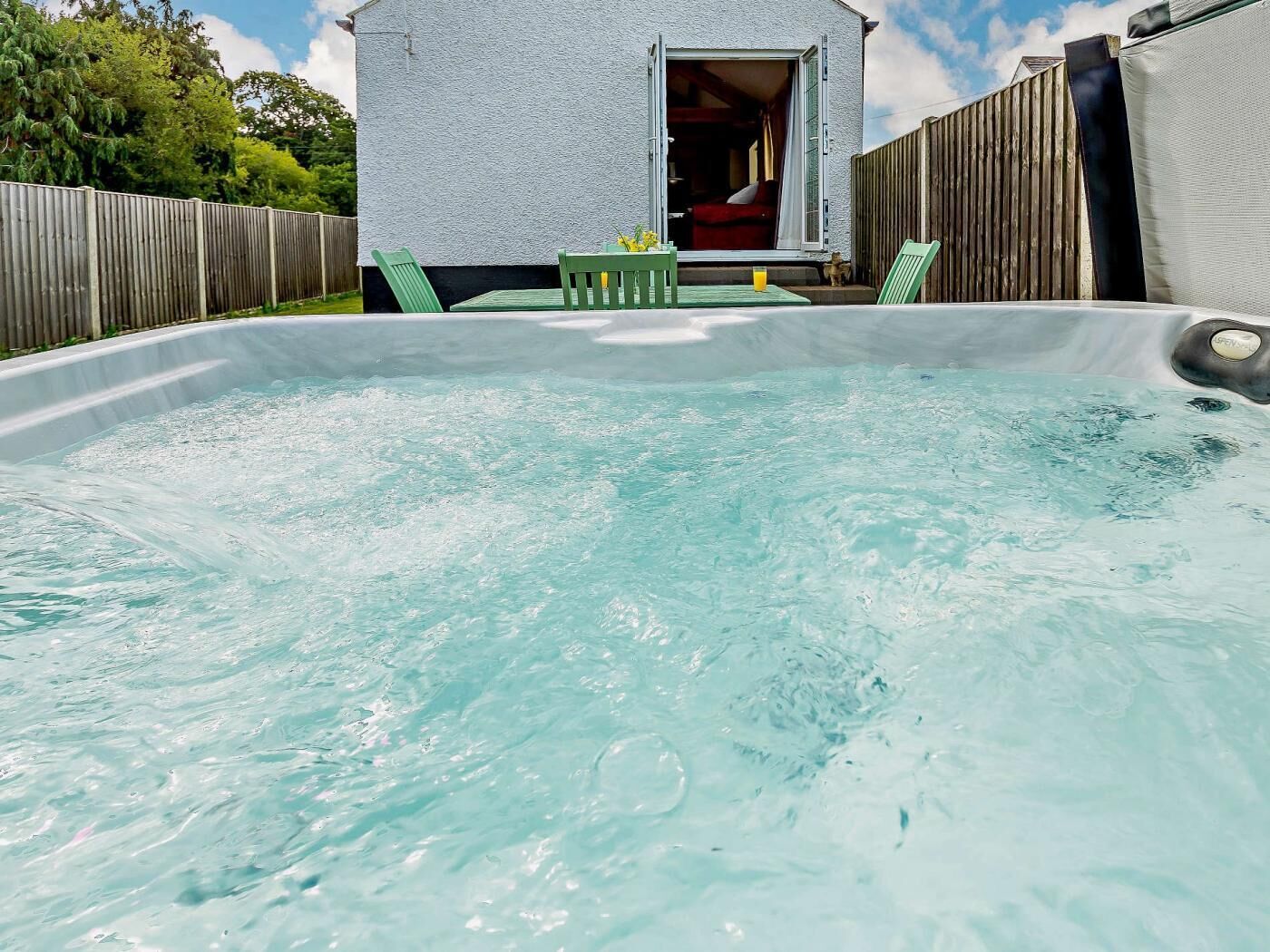 Ett bubbelbad med ett trädäck och ett litet hus i bakgrunden.