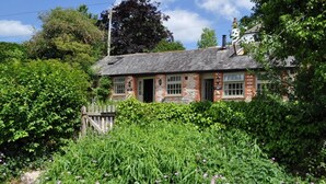 Un bâtiment traditionnel en briques, doté d’un toit en pente, d’une clôture en bois et d’un jardin où poussent diverses plantes et fleurs.