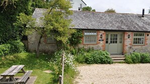 Un bâtiment rustique en pierre, avec une allée en gravier et une table de pique-nique en bois.