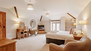 Ein Schlafzimmer mit einem Bett, Nachttischen, einem Fernseher, einem Sessel, einem Schreibtisch und einem großen Spiegel.